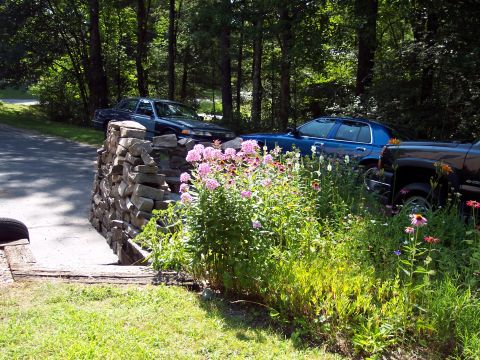 2001 Ford Crown Victoria - A 2001 Ford Crown Victoria is visible alongside other vehicles in a natural setting with a stone wall and blooming flowers.