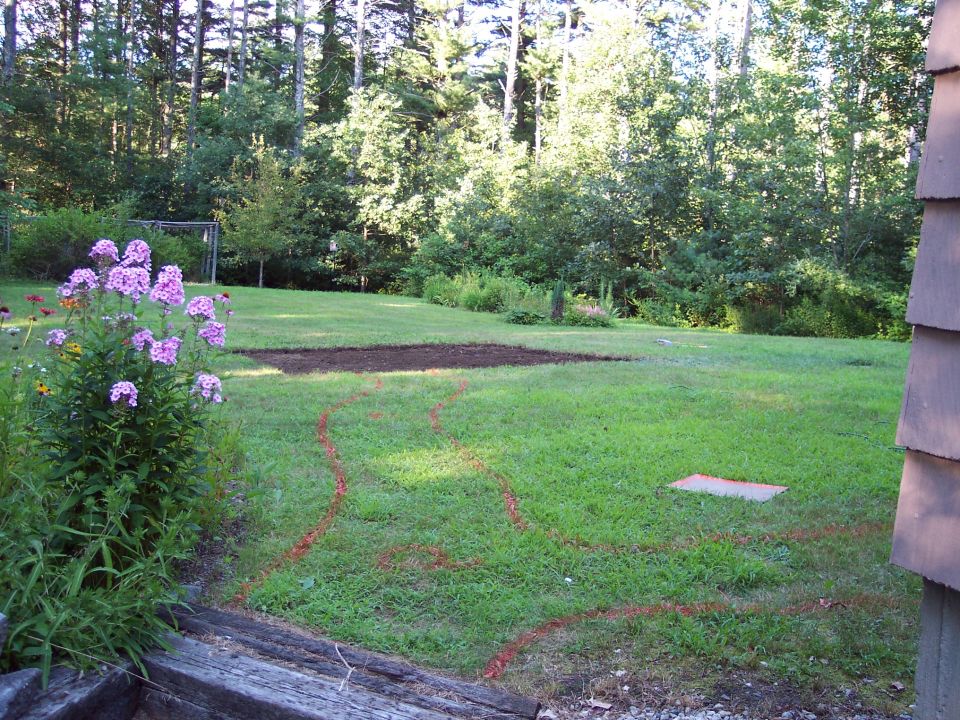 Backyard with a patch of tilled soil and red spray paint lines on the grass. Flowers are in the foreground