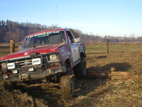 1978 Ford Bronco - A red Ford Bronco navigates a muddy off-road course, with a club sticker visible on the windshield.