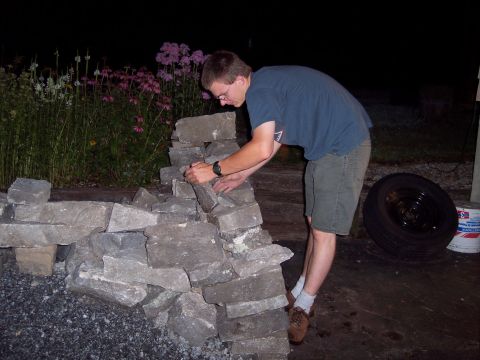 2001 Ford Crown Victoria - Man working on a stone wall construction project outdoors at night, with flowers in the background.