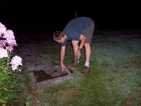 2001 Ford Crown Victoria - A person works on a stone path at night, with pink flowers in the foreground.
