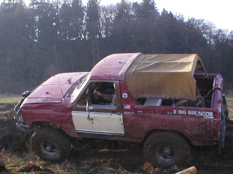 1978 Ford Bronco - A red 1978 Ford Bronco with a tan soft top is seen in a muddy field.
