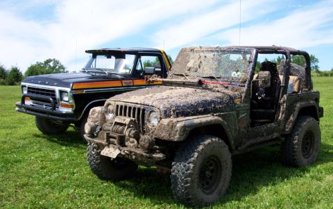 1978 Ford Bronco - Two off-road vehicles, a Jeep and a Ford truck, are parked on a grassy area after being driven through mud.