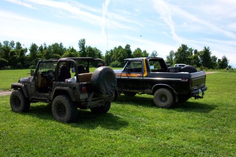 1978 Ford Bronco - A black 1978 Ford Bronco with an orange stripe is parked on a grassy field next to a Jeep.
