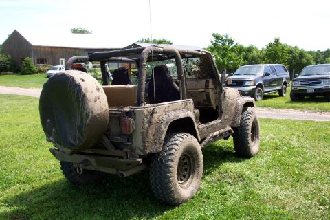 1978 Ford Bronco - A muddy Jeep Wrangler sits in a grassy field, with two other SUVs visible in the background.
