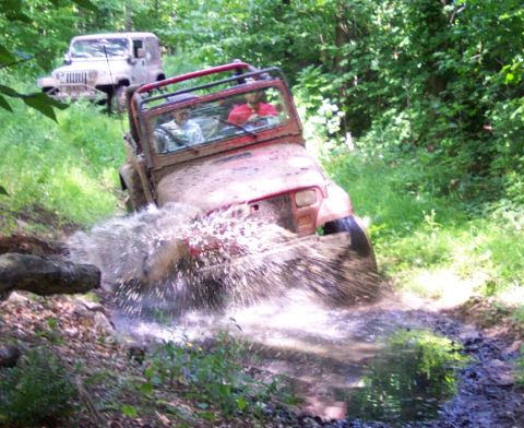 1978 Ford Bronco - Off-road vehicles splash through a muddy water crossing on a forest trail.