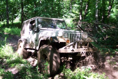 1978 Ford Bronco - A Jeep Wrangler navigates a muddy trail in a forest, kicking up dirt.
