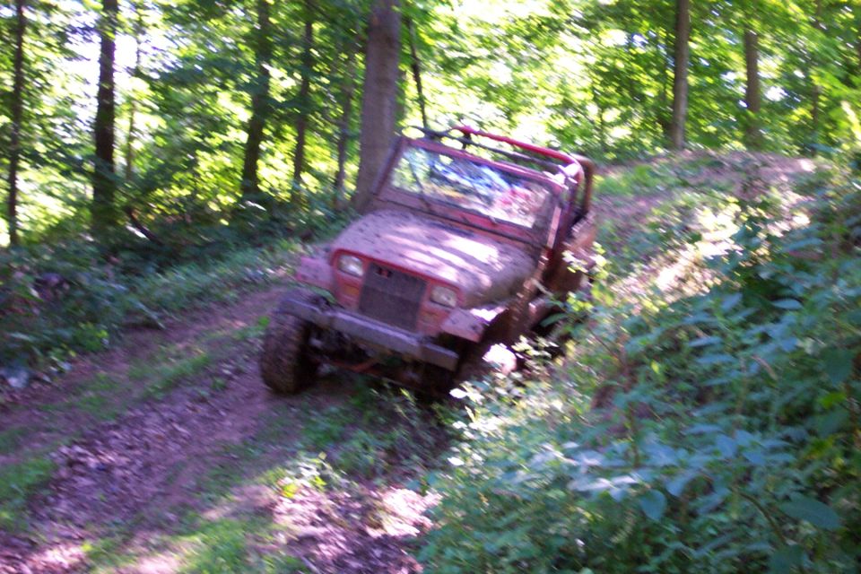 Mud-covered red off-road vehicle with a roll cage on a dirt path surrounded by trees