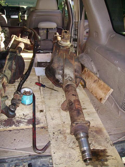 2000 Chevrolet Tahoe - Two rusty rear axle assemblies and tools are laid out on wooden planks inside a vehicle.