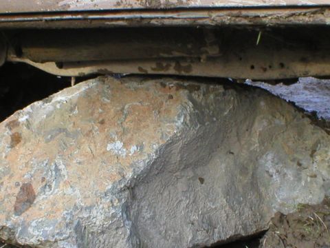 1978 Ford Bronco - A large rock is lodged under the frame of a vehicle, obscuring the view of the undercarriage.