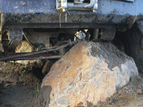 1978 Ford Bronco - Vehicle chassis is stuck on a large rock, with mud and dirt visible around it.