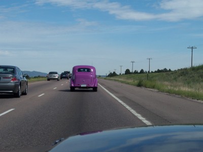 1972 Ford Ranchero - A purple vintage car travels down a highway on a sunny day.