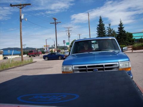 1972 Ford Ranchero - A blue Ford pickup truck is parked in a lot, with other vehicles visible in the background under a partly cloudy sky.