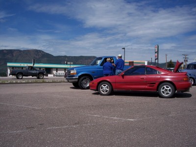 1972 Ford Ranchero - A red sports car and a blue pickup truck are parked in a lot with mountains in the background.