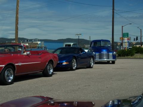 1972 Ford Ranchero - A blue 1950s pickup truck is parked behind a dark blue sports car and a red convertible in a parking lot.