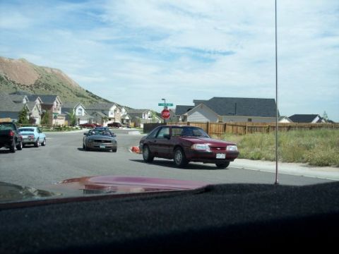 1972 Ford Ranchero - Several cars drive down a street in a residential area with a mountain in the background.