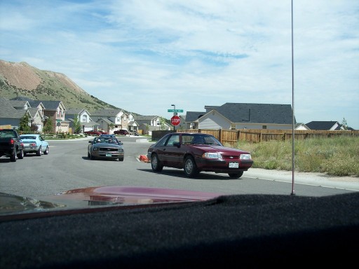 Red coupe with a license plate visible, driving on a suburban street