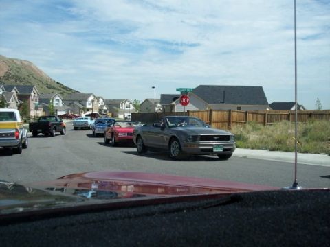 1972 Ford Ranchero - A convoy of vehicles travels down a residential street under a partly cloudy sky.