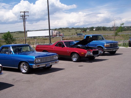 Red 1970s Ford Ranchero with hood open parked next to a blue 1960s Chevrolet Chevelle and a blue Ford pickup truck