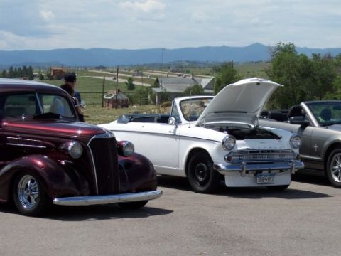 1972 Ford Ranchero - A white convertible is parked with its hood open, alongside other vehicles at an outdoor event.