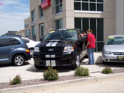 1972 Ford Ranchero - Black Ford F-150 pickup truck with racing stripes is parked outside a building with other vehicles.