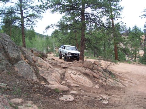 1978 Ford Bronco - A 1978 Ford Bronco navigates a , off-road path surrounded by pine trees and large rock formations.