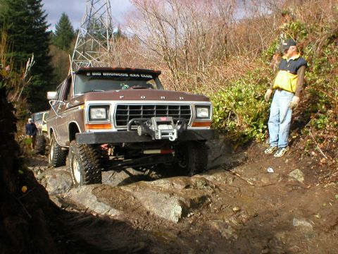 1978 Ford Bronco - A 1978 Ford Bronco navigates a challenging, rocky off-road trail with a bystander observing.