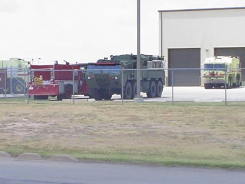 1981 Ford Bronco - A collection of specialized vehicles, including military trucks and fire engines, are parked outside a large building.