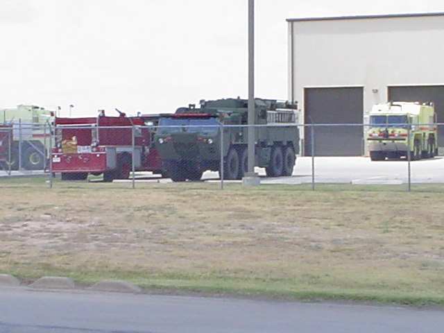 Several large trucks, including military and fire fighting vehicles, parked near a building