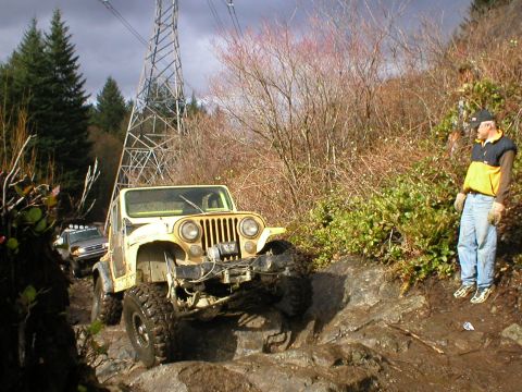 1978 Ford Bronco - A yellow Jeep CJ-5 navigates a rocky trail, with a second vehicle visible in the background.