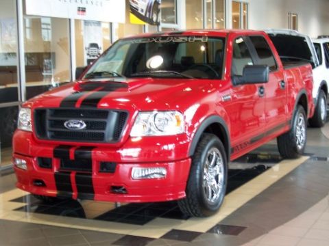 1972 Ford Ranchero - A red Ford F-150 pickup truck with black racing stripes is parked indoors next to other vehicles.
