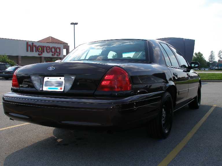 Black Ford Crown Victoria sedan on black steel wheels with doors open in a store parking lot