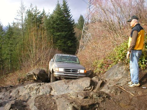 1978 Ford Bronco - A gray pickup truck is shown navigating a challenging rocky off-road trail, with a person observing the action.