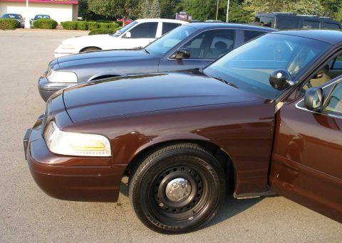 1998 Ford Crown Victoria - A brown 1998 Ford Crown Victoria is parked next to two other sedans, showing its 3/4 front profile.