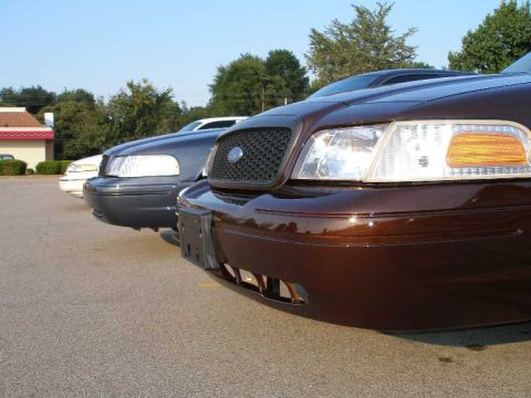 1998 Ford Crown Victoria - Several Ford Crown Victorias are parked in a lot on a sunny day.