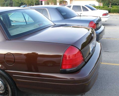 1998 Ford Crown Victoria - Three Ford Crown Victorias are parked in a lot, with the closest one being brown and the others silver and white.