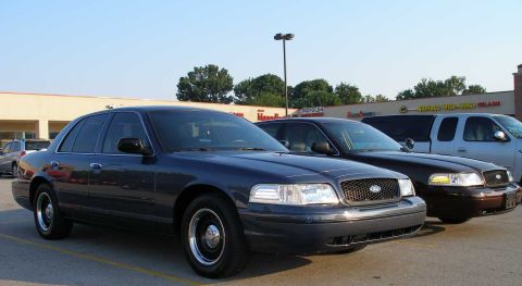 1998 Ford Crown Victoria - Three sedans and a pickup truck are parked in a lot in front of a strip mall.