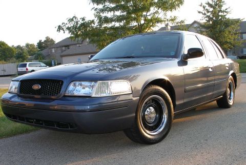 1998 Ford Crown Victoria - A dark gray 2003 Ford Crown Victoria is parked outside on a sunny day, with a white van visible in the background.