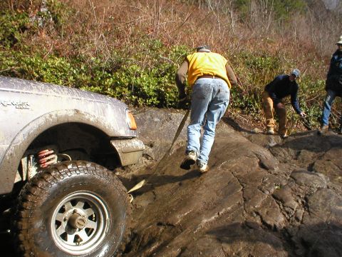 1978 Ford Bronco - Several people are navigating a challenging off-road course with a silver SUV stuck on a rocky incline.