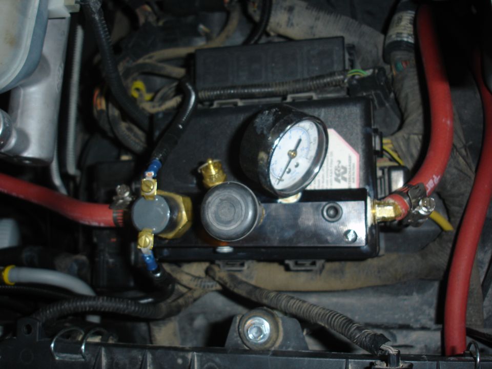 Engine-bay-mounted brass valve manifold with round pressure gauge and red lines