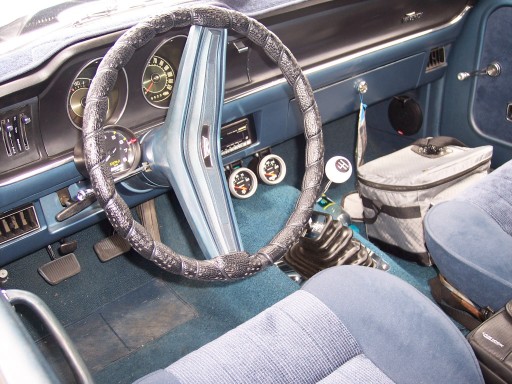 Interior shot of a car with a blue dashboard, steering wheel, and seats. Gear shift and a cooler are visible