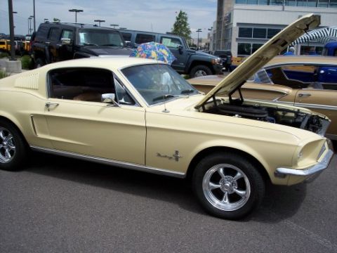 1972 Ford Ranchero - A cream 1967 Ford Mustang is displayed with its hood open, parked alongside other vehicles at an outdoor event.