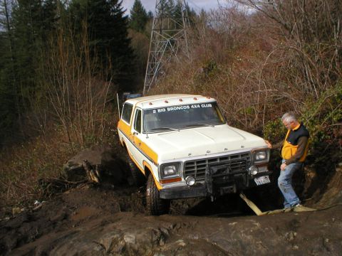 1978 Ford Bronco - A man watches as a 1978 Ford Bronco navigates a challenging, muddy off-road course.