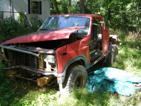 1984 Ford Bronco - This red pickup truck is in disrepair, with its hood up and doors removed, parked outdoors.