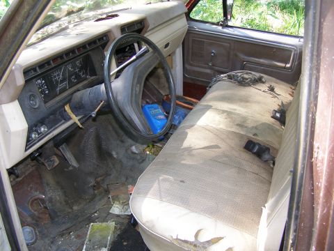 1984 Ford Bronco - The interior of a dilapidated 1980s pickup truck cab, with visible wear and tear on the seats and dashboard.