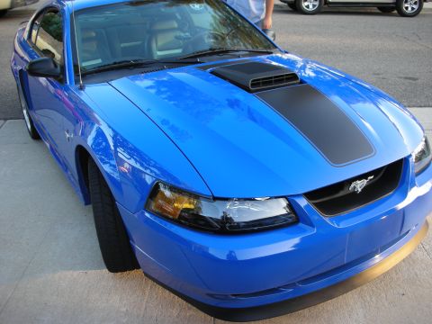 1998 Ford Crown Victoria - Front three-quarter view of a blue Ford Mustang with a black hood stripe and scoop and the chrome running-horse grille badge.
