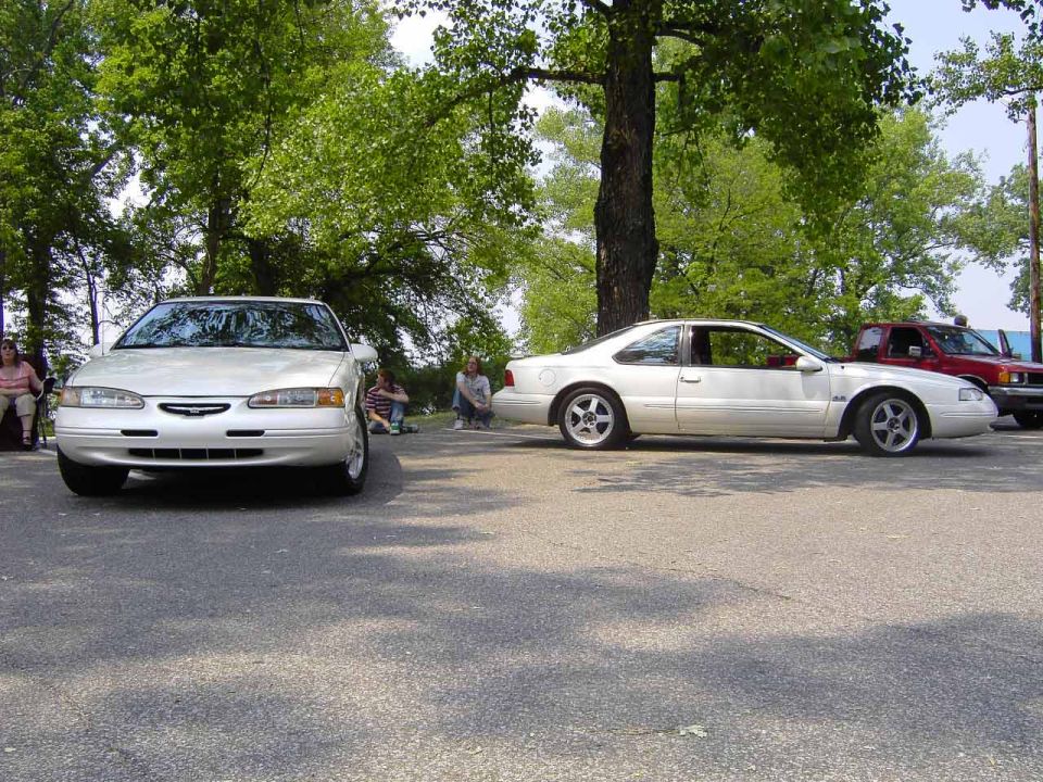 White Ford Thunderbird parked next to another car, with people sitting nearby
