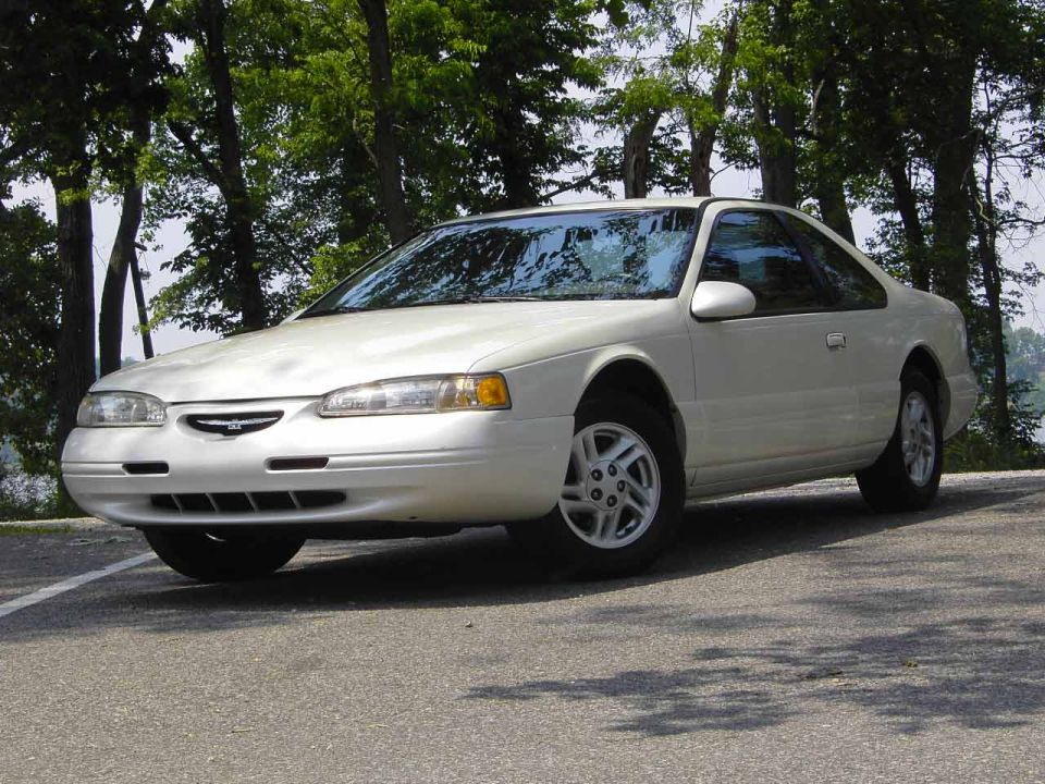 White 1996 Ford Thunderbird coupe parked on asphalt, trees in background
