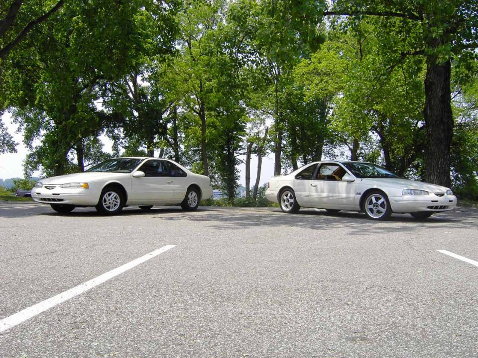 Two white 1996 Ford Thunderbirds parked on asphalt with trees in the background
