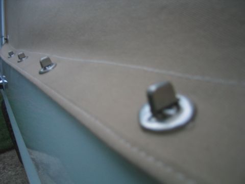 1996 Ford Bronco - Extreme close-up of the lower hem of a tan vinyl soft top, showing the stitched edge and a row of chrome lift-the-dot fastener studs mounte…